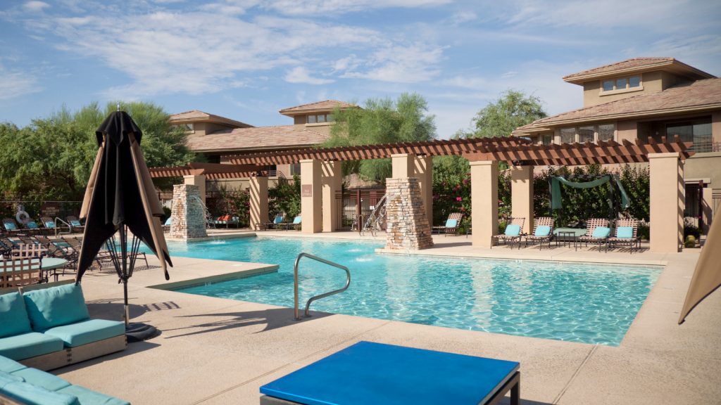 Community swimming pool with lounge chairs, a table, and an umbrella.
