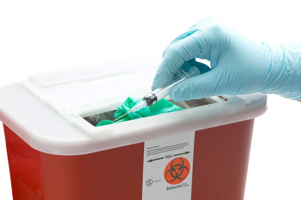 Gloved hand putting a needle in a Sharps Container
