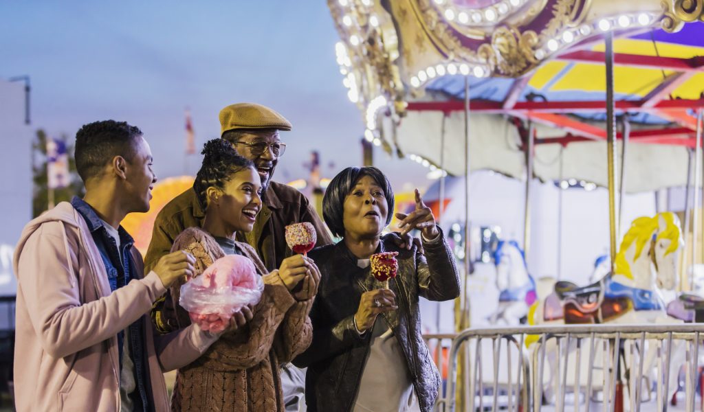 Senior couple, adult grandchildren at amusement park.