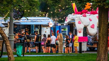 People queue at a street food truck. City park on a summer evening.